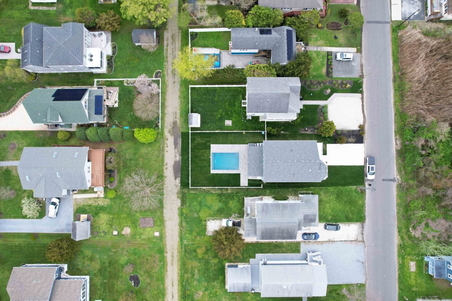 High-altitude aerial photograph of a residential neighborhood shows one property in the center frame with a small completed rectangular in-ground pool visible in the backyard, surrounded by lawn and adjacent single-family homes.